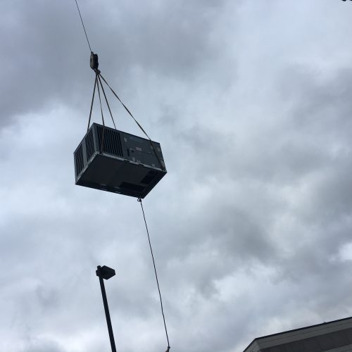The HVAC installation team at Accurate Heating & Cooling hoists an air conditioner into the air with a crane in Columbia, Mo.